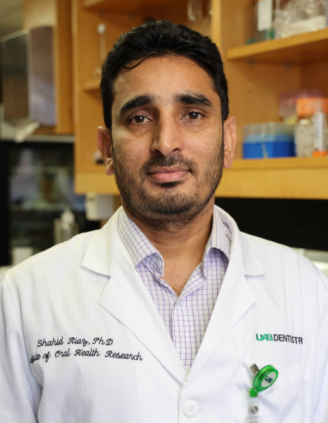 Man with black hair wearing a white coat in a lab setting